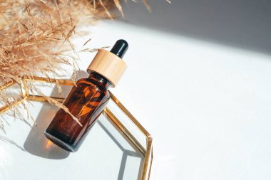 Kehribar cam şişe damlatıcısı pipeti, serum ya da ürün sunumu için cam tabakta gerekli yağ. Cilt makyajı ve kır çiçekleri. Yüz bakımı için güzellik konsepti