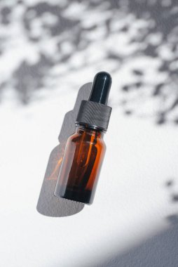 Amber bottle with cannabis oil used for medical purposes. White background with daylight and flowers shadows. Soothing cbd oil. Alternative Medicine