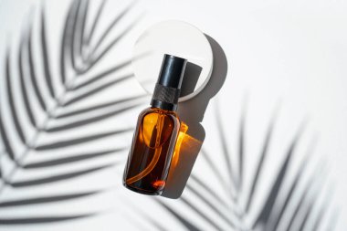 Amber pump bottle with serum, tonic or essential oil on concrete podium. White background with daylight with palm shadows. Beauty concept for face and body care