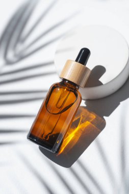 Amber dropper bottles with serum, tonic or essential oil on concrete podium. White background with daylight with palm shadows. Beauty concept for face and body care
