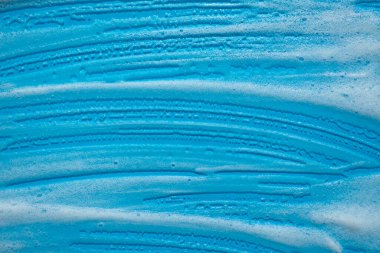 Mavi arka planda köpük örneği. Köpüklü sabunlu sıvı doku. Doğal güneş ve gölgeler. Üst görünümde cilt bakım temizleme kozmetiği.