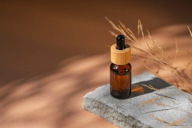 Bambu kapaklı ve kuru bitkili kehribar cam damlası. Ürün sunumu için gri beton podyumda bir şişe. Cilt bakım ürünleri ve kır çiçekleri. Güzellik konsepti