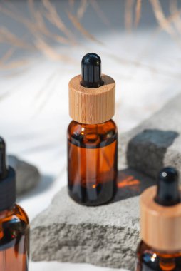 Bambu kapaklı ve kuru bitkili kehribar cam damlası. Ürün sunumu için gri beton podyumda bir şişe. Cilt bakım ürünleri ve kır çiçekleri. Güzellik konsepti