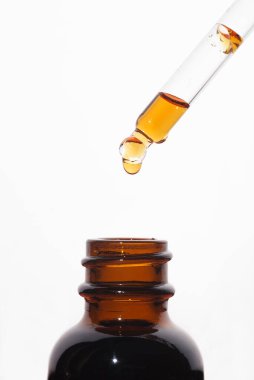 A drop of liquid falling from a pipette into an amber bottle. Skincare products, natural cosmetic on white background. Beauty concept for face and body care.