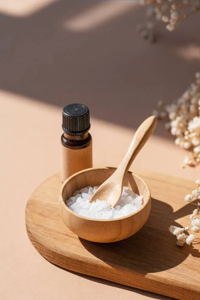 Amber bottles with craft label filled essential oil and bowls filled with white bath sea salt on wooden tray. Beauty concept for face and body care. Natural cosmetic and dry flowers