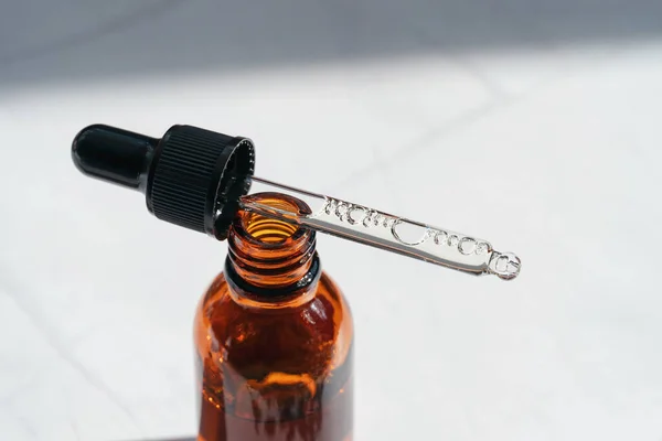 Open amber bottle with dropper pipette with serum or essential oil and shadows. Skincare products, natural cosmetic on white background. Medicine and beauty concept for face and body care.