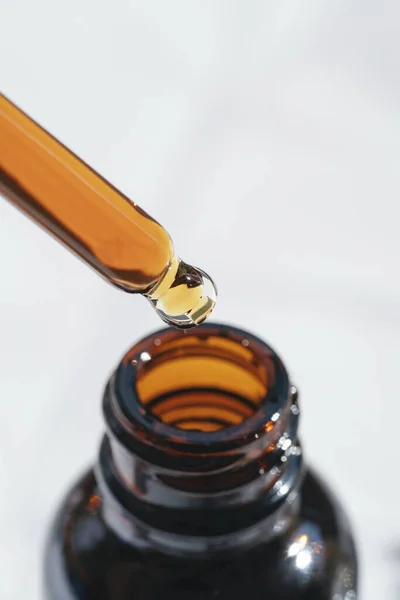 Open amber bottle with dropper pipette with serum or essential oil. Skincare products, natural cosmetic on white background. Medicine and beauty concept for face care. Selective focus in the center