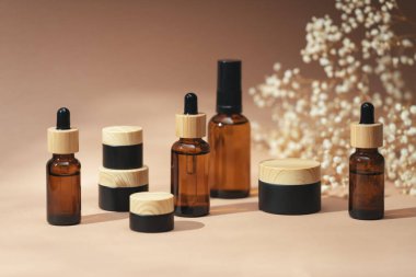 Kehribar şişelerinde damla pipeti ve kavanozlarda krema, serum ya da gerekli yağ var. Bej arka plan gün ışığı ve güzel çiçekler. Yüz ve vücut bakımı için güzellik konsepti