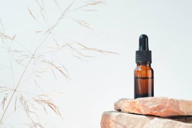 Kehribar şişesinde serum, tonik ya da taş podyumda gerekli yağ var. Gri arka plan. Yüz ve vücut bakımı için güzellik konsepti. Cilt ürünleri, doğal kozmetik ürünleri..