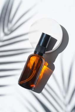 Amber pump bottle with serum, tonic or essential oil on concrete podium. White background with daylight with palm shadows. Beauty concept for face and body care