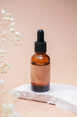 Kehribar cam damlatıcı şişesinde serum ya da gerekli yağ var. Bej arka plan, gün ışığı ve güzel çiçekler. Cilt doğal kozmetik. Yüz ve vücut bakımı için güzellik konsepti