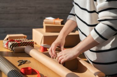 Hediye paketi ekolojik paketleme. Genç bir kadın Kraft hediye kutusunda fiyonk yapıyor. Ahşap bir masada kırmızı iplikle. Kutlama için hediye paketleme ve hazırlama.