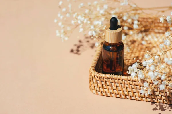 Amber bottle with dropper pipette in a wicker basket. Beige background with daylight and beautiful shadows. Skincare serum or essential oil natural cosmetic. Beauty concept for face and body care