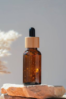 Amber dropper bottle with serum or gel on stone podium. Grey background. Beauty concept for face and body care. Skincare products, natural cosmetic.