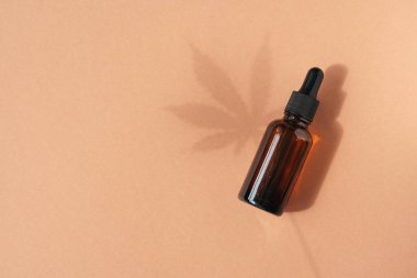 Amber glass dropper bottles with cannabis oil used for medical purposes on beige background. Daylight and the shadow of a hemp leaf. Soothing cbd oil. Alternative Medicine. Copy space