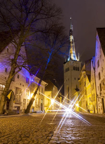 Calle iluminada en el casco antiguo de Tallin, Estonia por la noche. Iglesia de San Olaf en el fondo . — Foto de Stock