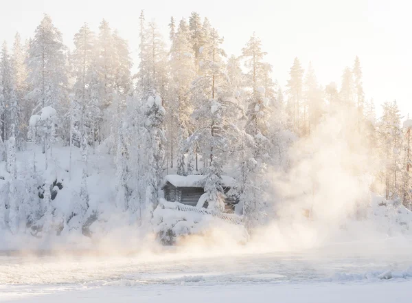 Small log cabin behind vaporing river — Stock Photo, Image