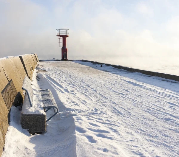 Beacon and bench on snowy mole — Stock Photo, Image