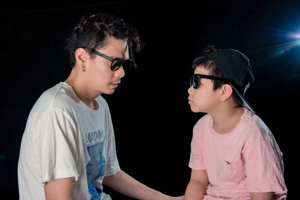 Mann Und Kleiner Junge Mit Sonnenbrille Sitzen Auf Dunklem Studiohintergrund — Stockfoto