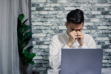 Evde masa başında dizüstü bilgisayarla çalışan kızgın bir işadamı.