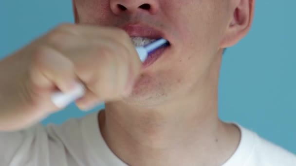 El hombre se cepilla los dientes con un cepillo de dientes de cerca sobre fondo azul. — Vídeo de stock