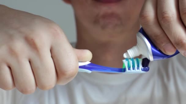 Ένα αρσενικό χέρι πιέζει οδοντόκρεμα σε ένα κοντινό πλάνο οδοντόβουρτσας. — Αρχείο Βίντεο