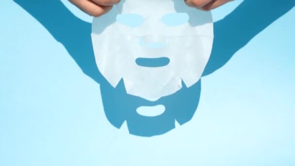 Mannelijke handen houden witte stof masker op blauwe achtergrond close-up. — Stockvideo