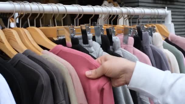 A man chooses sweater hanging on hangers in retail mall, close-up. — Vídeos de Stock