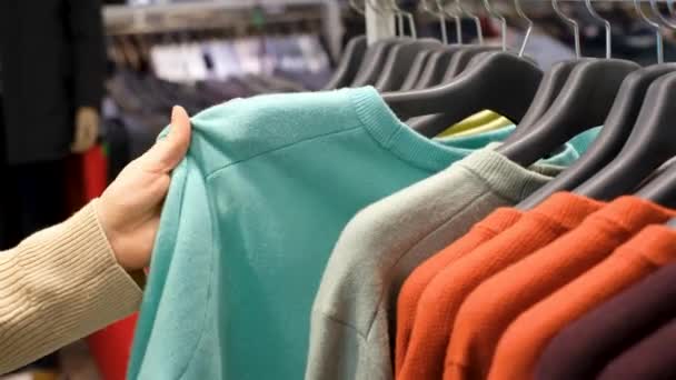 Chica elige la ropa que cuelga de la percha en la tienda de cerca. — Vídeos de Stock