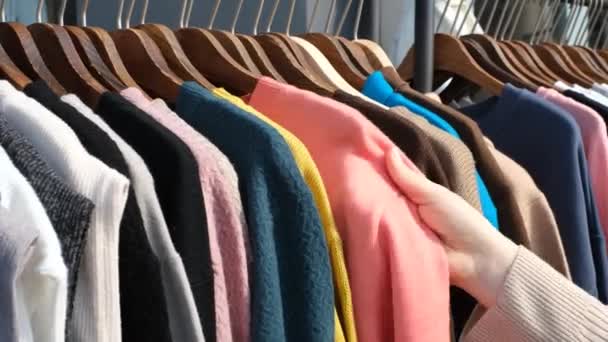 La mano femenina elige la ropa que cuelga de la percha de cerca. — Vídeos de Stock