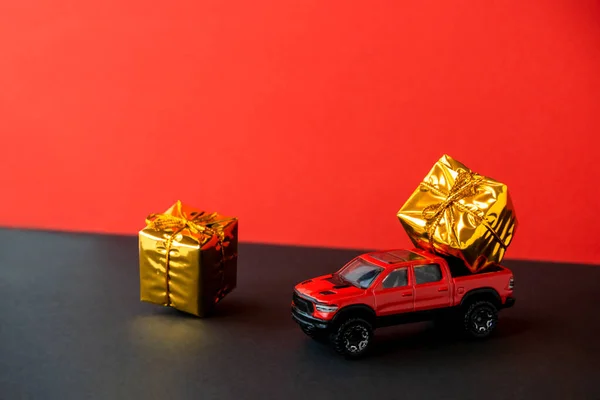 Red toy car SUV gift box on trunk close-up,two-tone black background,levitating festive packaging,bow.New Year,Christmas holiday automobile concept.Dealership prize drawing.Copy space.Auto delivery.