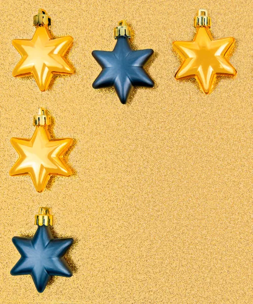 Closeup festive 5 Christmas tree toys,gold,dark gray stars,upper left border,shiny shimmering golden sequined backdrop.Christmas,New Year,birthday metal holiday decoration.Vertical banner,copy space.
