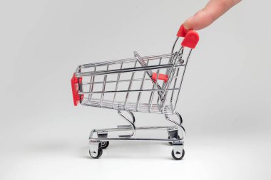 İnsan parmağı boş market alışveriş arabasını itiyor. Beyaz arkaplanda izole
