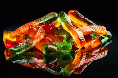 Yığınla sulu renkli jöle solucanları. Şekerleme. Yılanlar. Siyah üzerine.