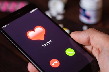 Kalp yetmezliğinin ilk çağrıları. Kalbinden seslen. Adam, ilaç ve hapların arka planında kalpten gelen bir aramayla telefonu bekletiyor. Sağlık kavramı