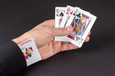 Konsept - kolunda joker kartı. Elinde karanlık arka planda kartları tutan bir adam..