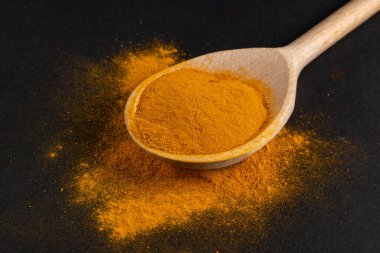 Koyu arkaplanda tahta kaşıkta zerdeçal tozu..