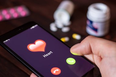 Sağlık konsepti. Kalp yetmezliğinin ilk çağrıları. Kalbinden seslen. Adam, ilaç ve hapların arka planında kalpten gelen bir aramayla telefonu bekletiyor. Tüm ekran grafikleri uydurma