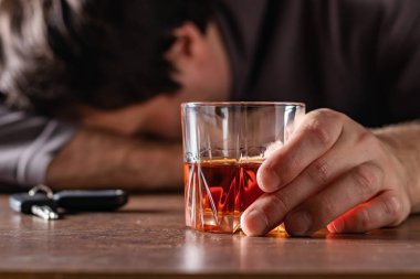 Alkolizm, alkol bağımlılığı ve insan konsepti. Bir bardak viskiyle masada yatan ya da uyuyan erkek alkolik. Masada duran otomatikten alınan anahtarlar.