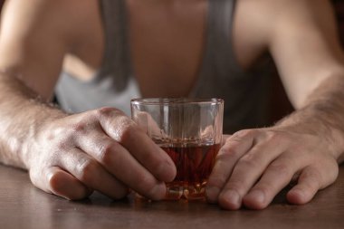 Alkolizm konsepti. Genç adam çok fazla alkol alıyor. Bir bardak viskiyle tişört giymiş alkolik..