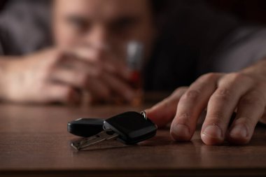 İçkili araba kullanmayın. Elinde cam alkol olan sarhoş bir adam arabanın anahtarlarını alıyor..