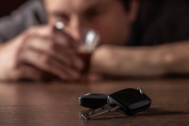 İçkili araba kullanmayın. Elinde cam alkol olan sarhoş adam arabanın anahtarlarına bakıyor..