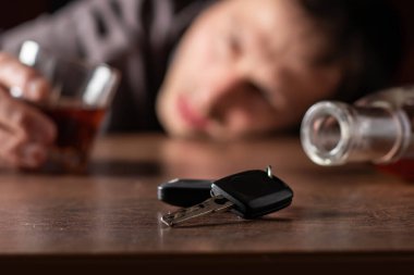 İçkili araba kullanmayın. Elinde cam alkol olan sarhoş adam arabanın anahtarlarına bakıyor..
