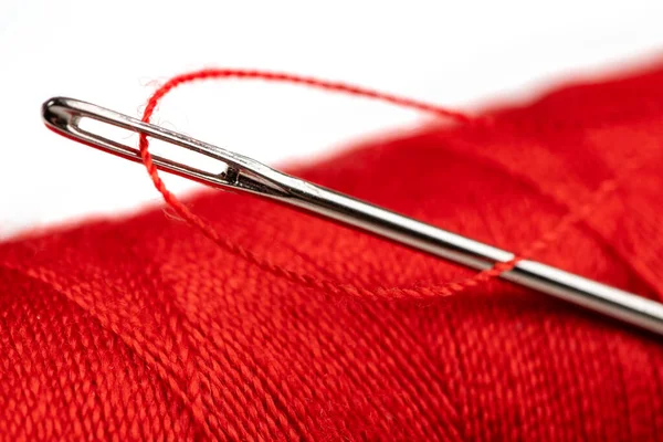 赤いポリエステル糸で針の目 背景に赤いポリエステルの縫製糸のスプール 選択的フォーカス ぼっけ — ストック写真