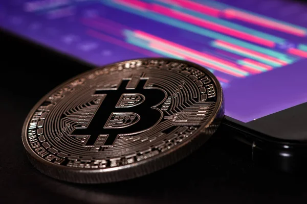 Bir akıllı telefon ekranının arka planında kripto para piyasası dalgalanmaları grafiği olan bitcoin para