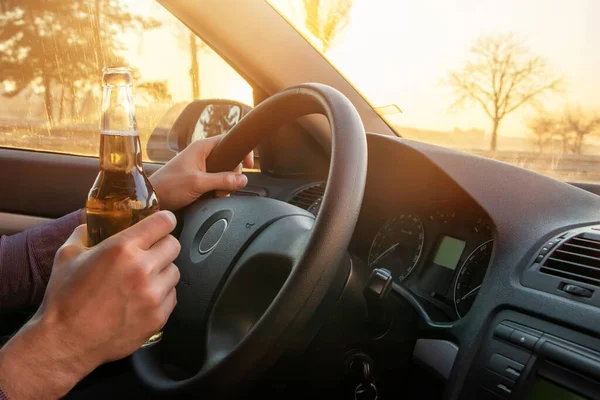 Gün batımında araba kullanırken alkol alan bir adam..