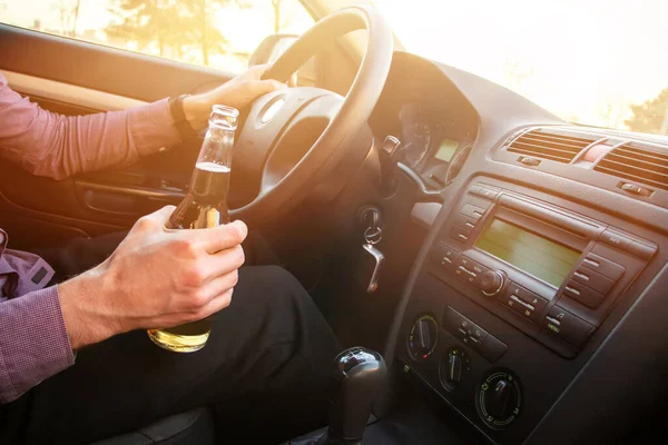 Gün batımında araba kullanırken alkol alan bir adam..