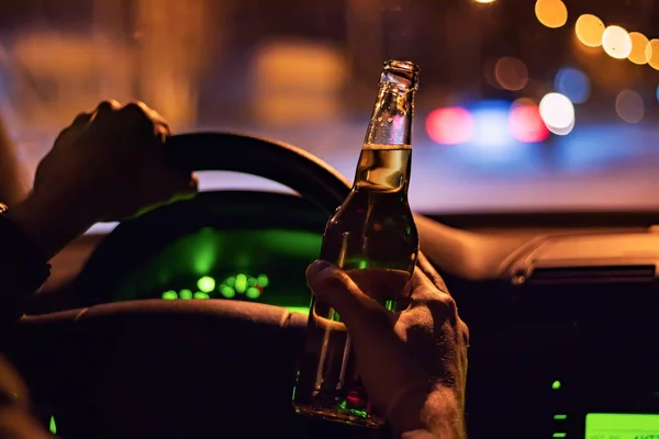 Man drink beer while driving at night in the city. Dangerously driving.