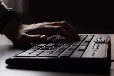 Karanlıkta bir adamın elleri klavyede. Şifre kırılıyor. Seçici odak.