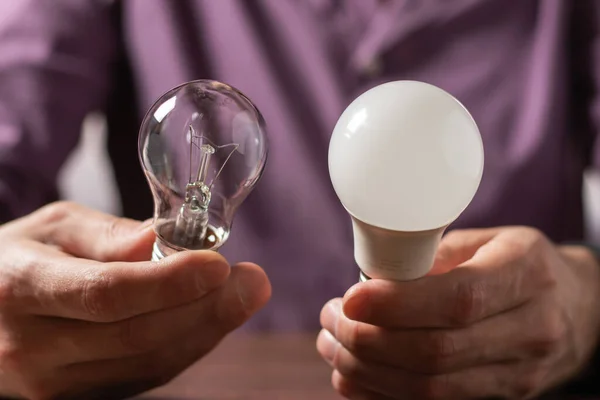 Two lamps in the hands of a man. Incandescent light bulb and LED light bulb in your hands. Close-up.